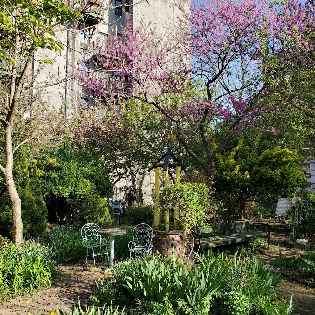 The garden in spring — flowering redbud, iron chairs, a brick wall behind.